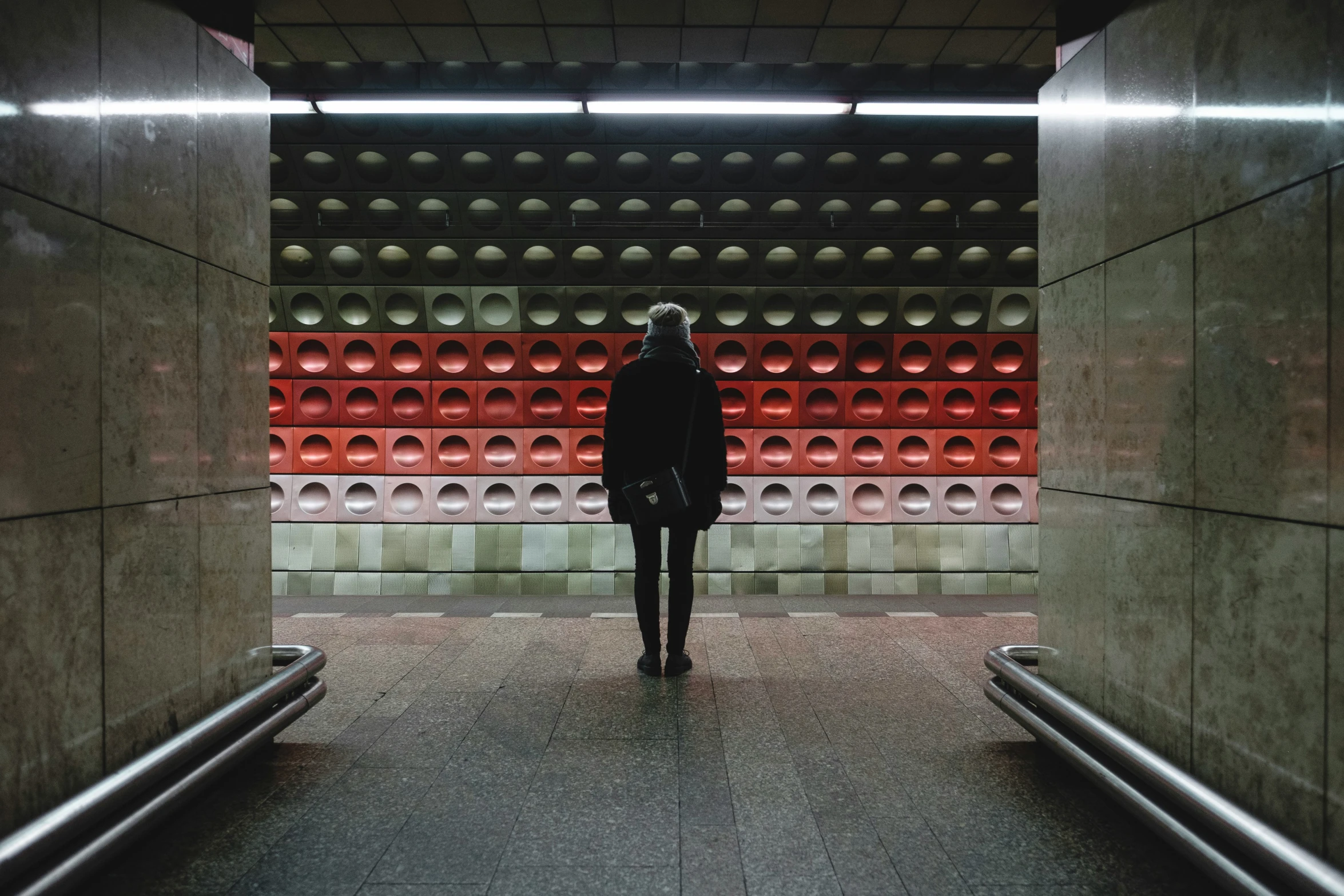 a person is standing in a tunnel by a row of red bottles