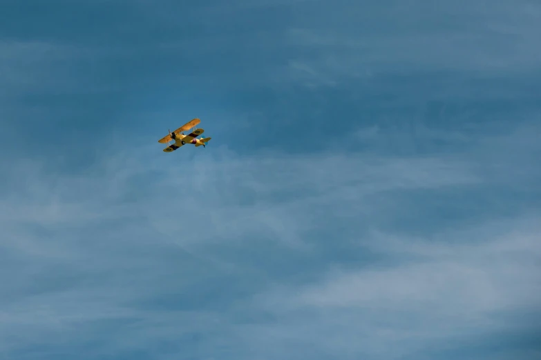 an old yellow airplane flying in a clear blue sky