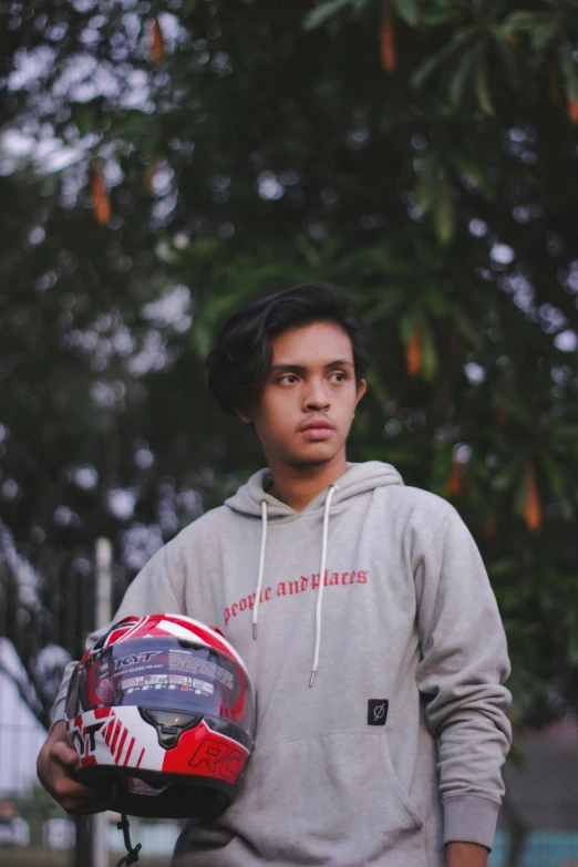 a boy in hood and sweatshirt holding a motorcycle helmet