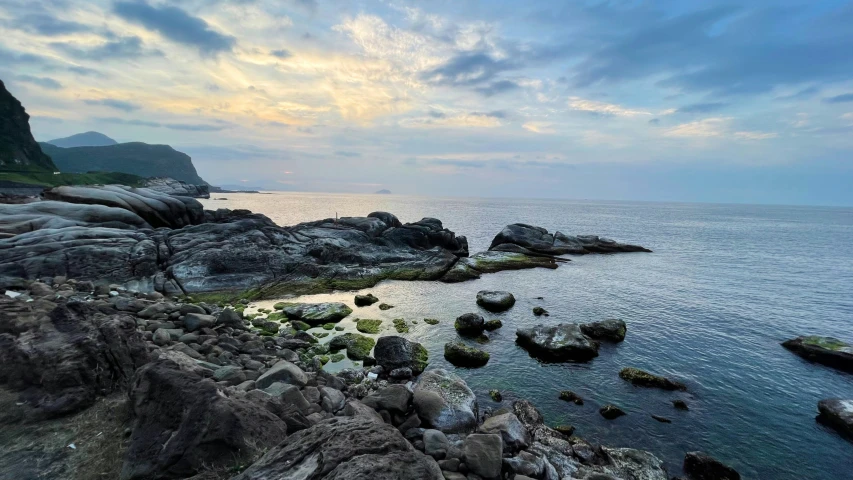 a rocky beach near the ocean with some clouds