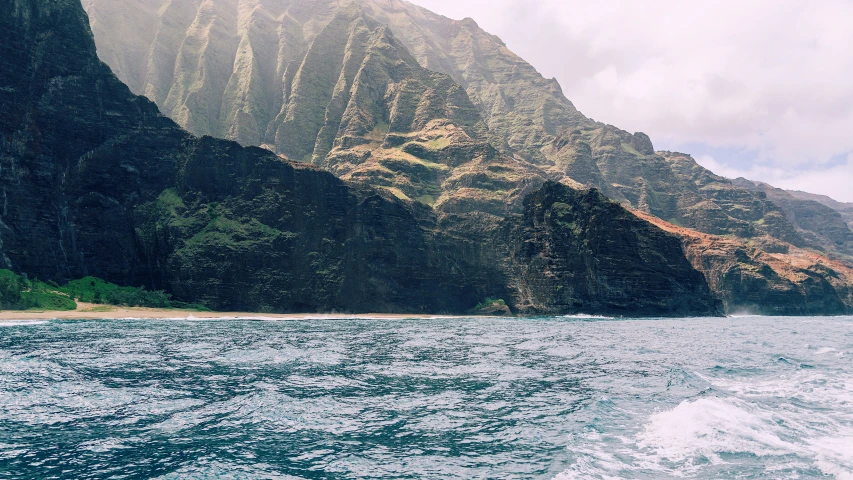 a boat sailing in the water next to a mountain