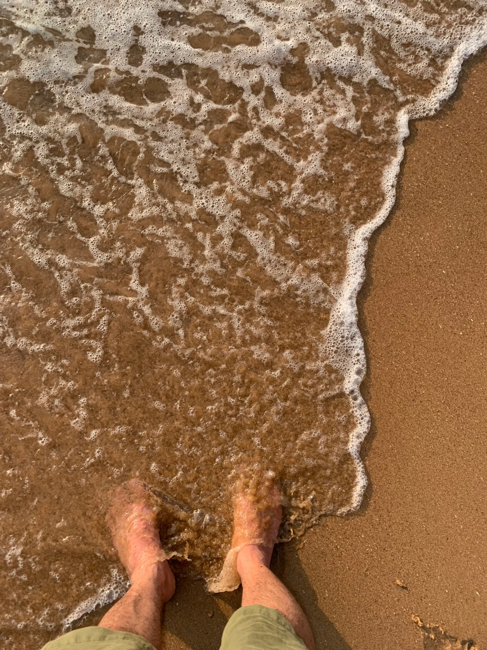 a person's legs are seen at the edge of the water on a beach