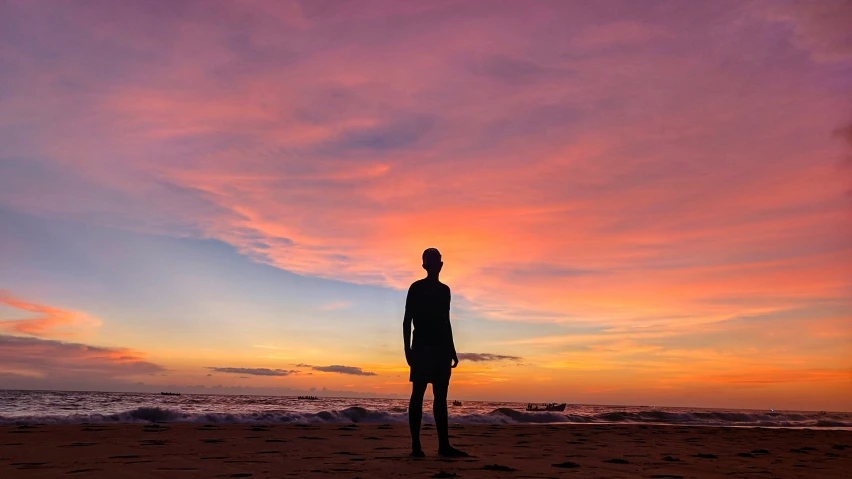 there is a man standing on the beach under a colorful sunset