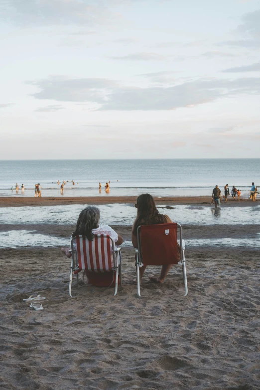 two people sitting in red and white chairs facing the water