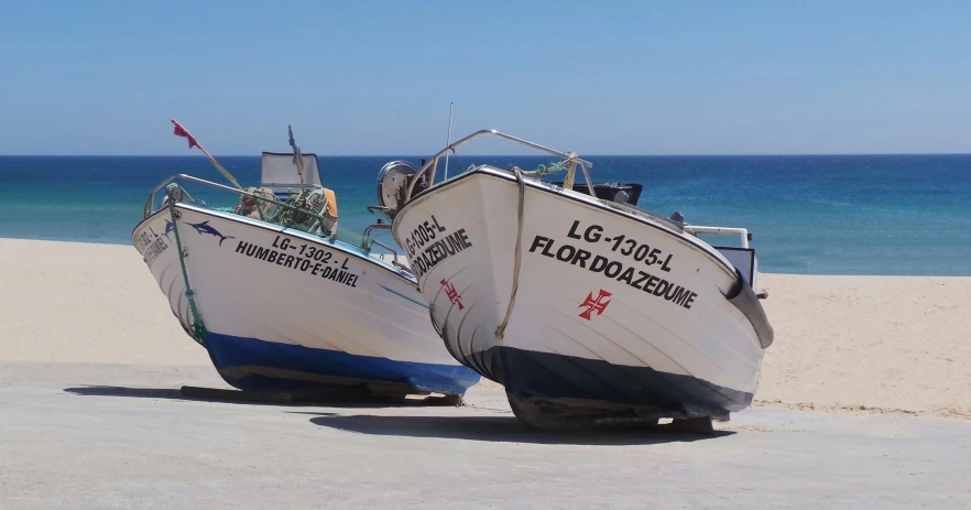 two boats sitting on the sand near the ocean