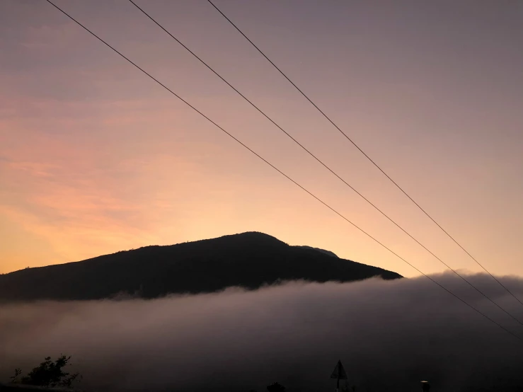 the sun sets over a large mountain while power lines are visible