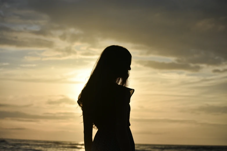 a woman is silhouetted against a sky as she stands on the beach at sunset