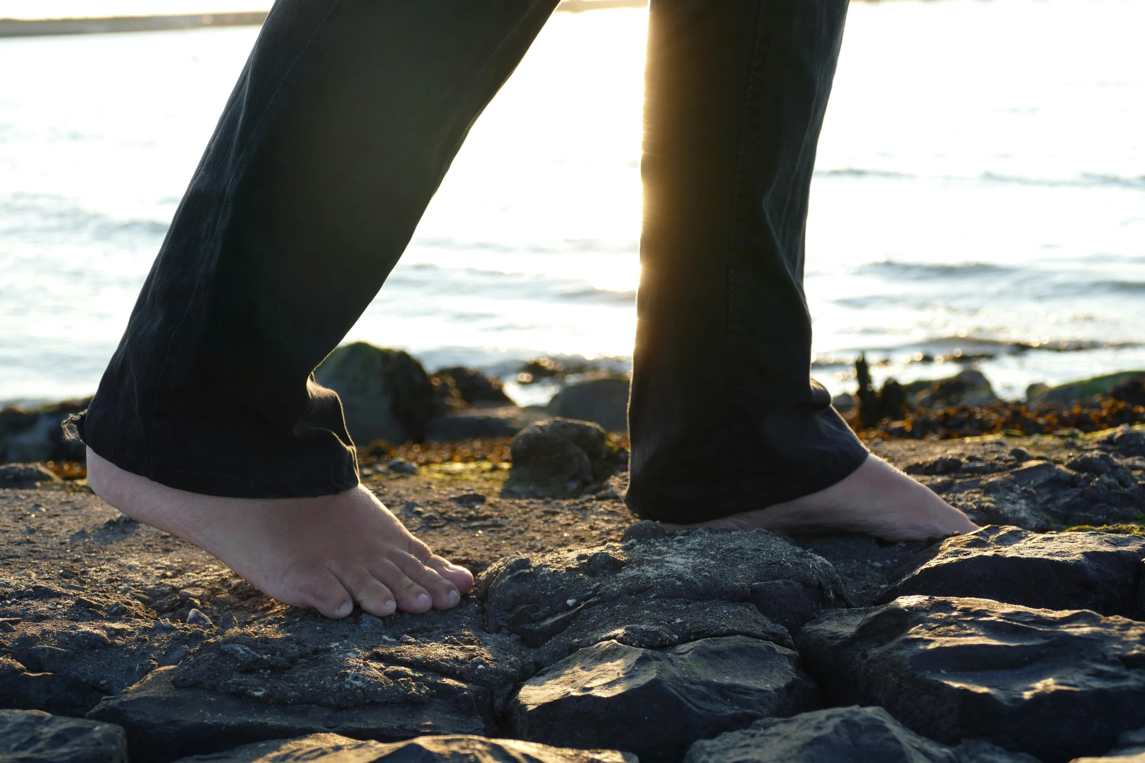 a persons feet standing on rocks near the water