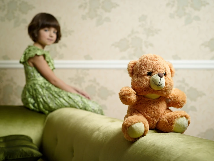 a little girl sitting on a bed next to a large teddy bear