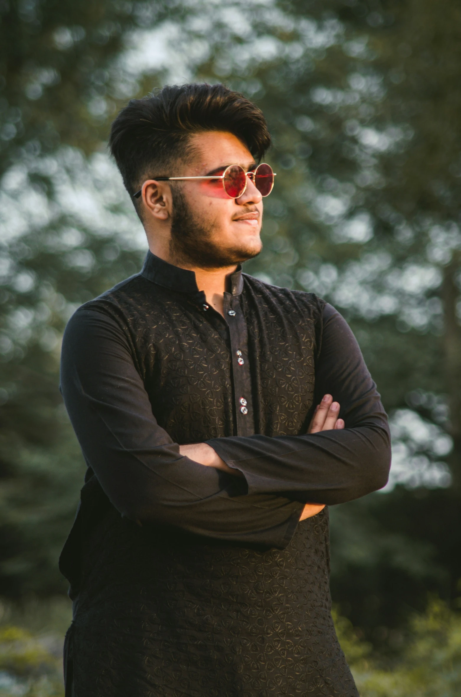 man wearing sunglasses standing outside with his arms crossed