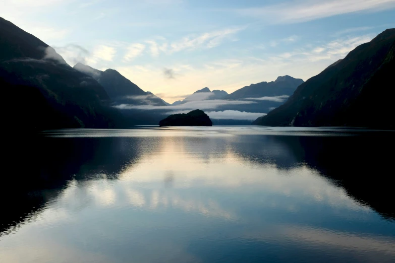 a body of water surrounded by mountains under a cloudy sky