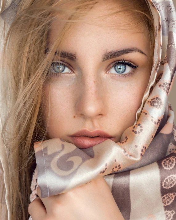 a close - up po of a blonded woman with blue eyes and her hand under the chin