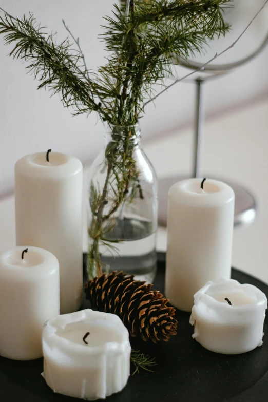 white candles and pine cones are arranged on a black tray