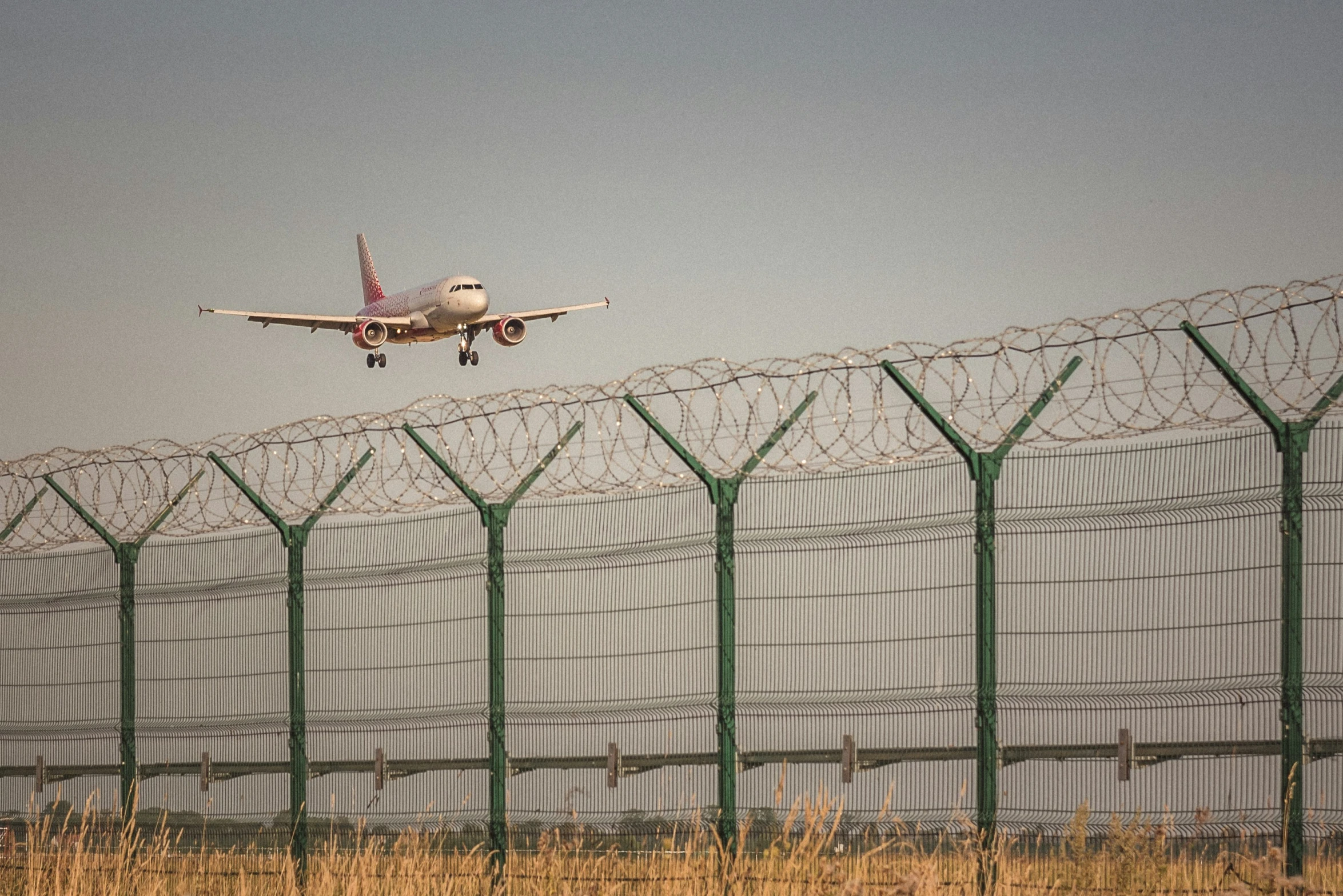 a airplane flying low to the ground on a fenced off runway