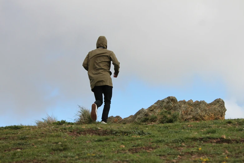 man running on the top of a hill under a cloudy sky