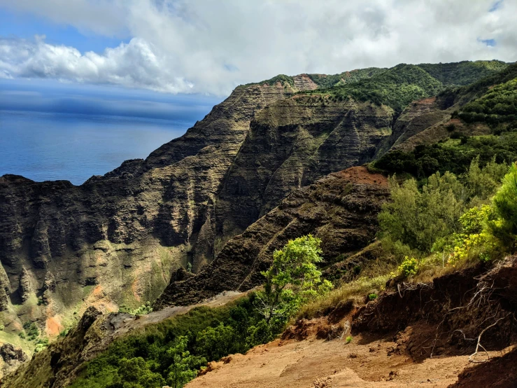 mountain overlooking a blue ocean below clouds and trees