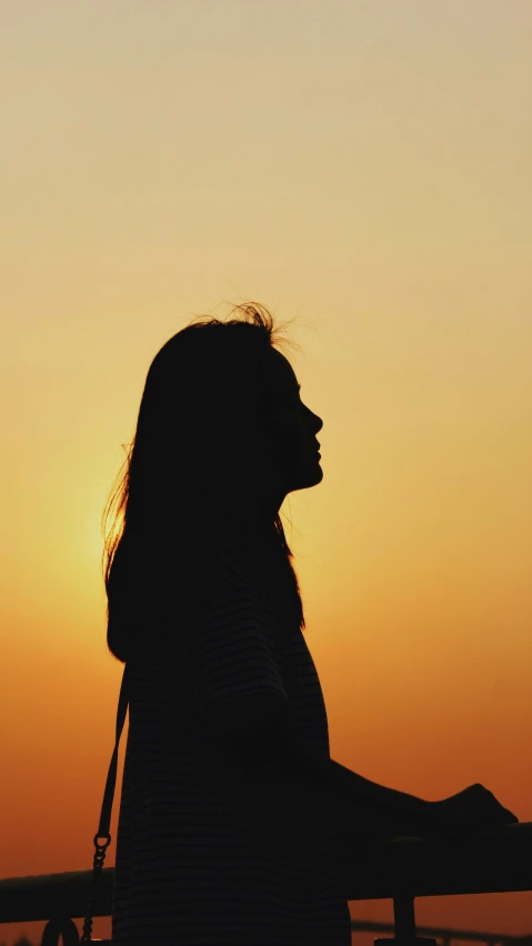 a girl sitting on a rail looking at the sun