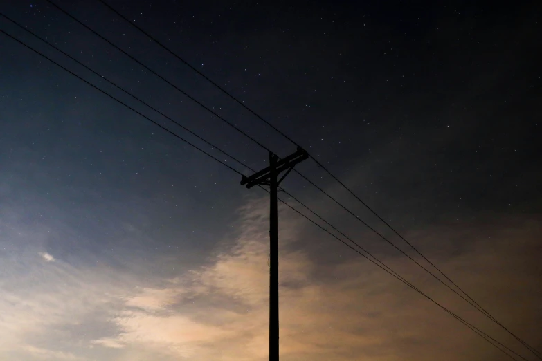 there is a pole with power lines that are against a dark background