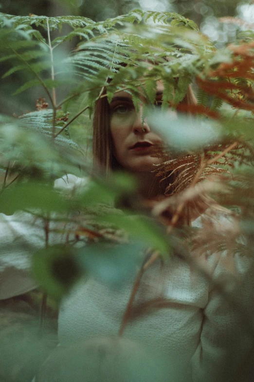 a woman that is peeking out from behind some plants