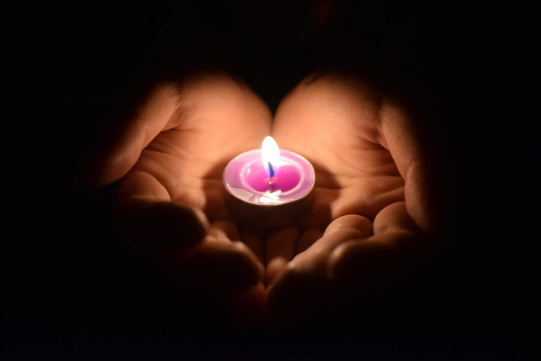 some hands holding a lit candle that is in the dark