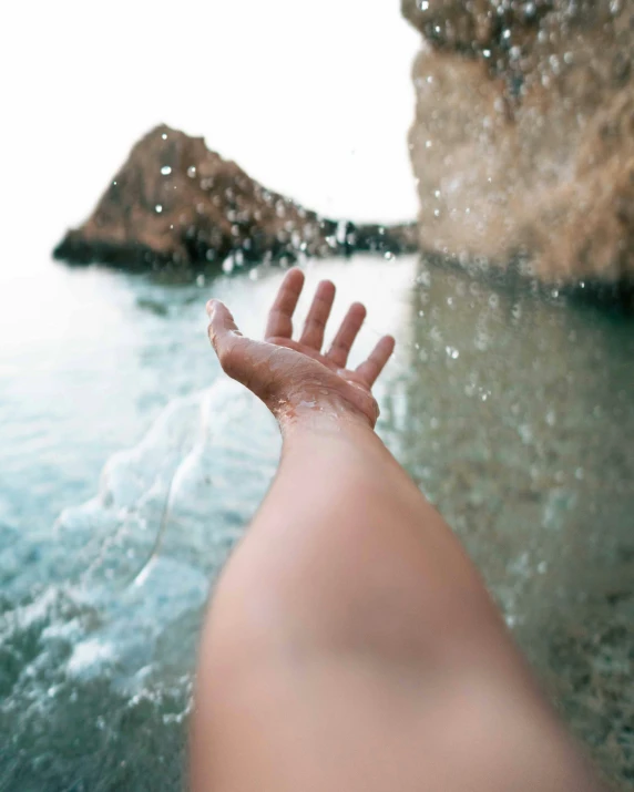 a person is sitting by the water reaching out