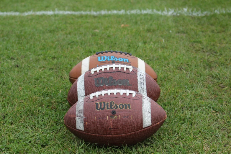 two footballs on the ground with one leaning over the other