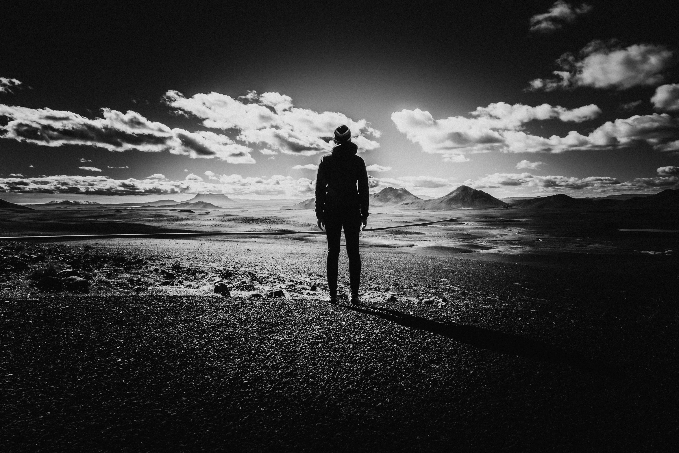 person standing on black beach with cloudy sky