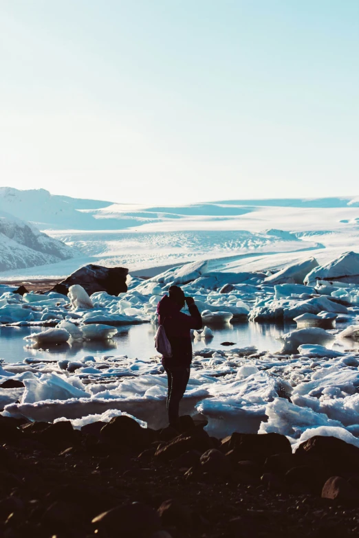 two people walk down the beach from some large glacier