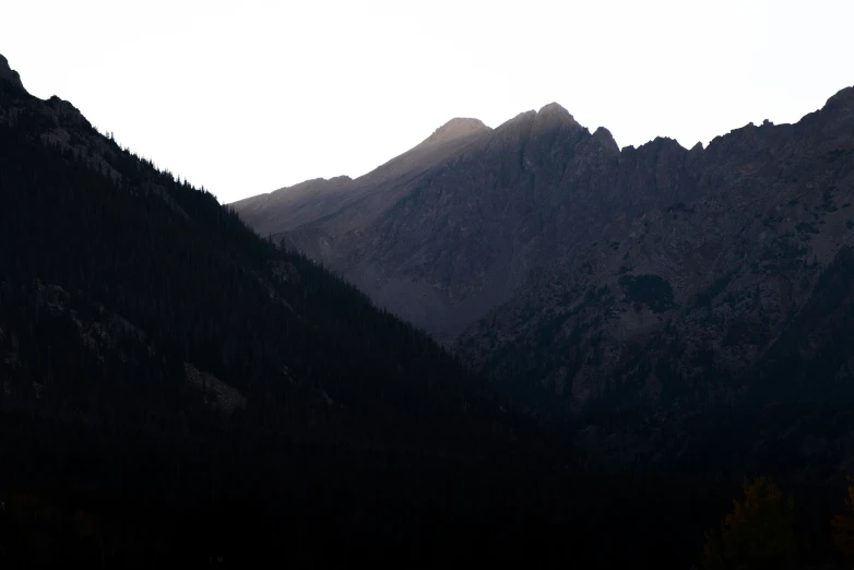 silhouettes of trees on mountains with cloudy sky