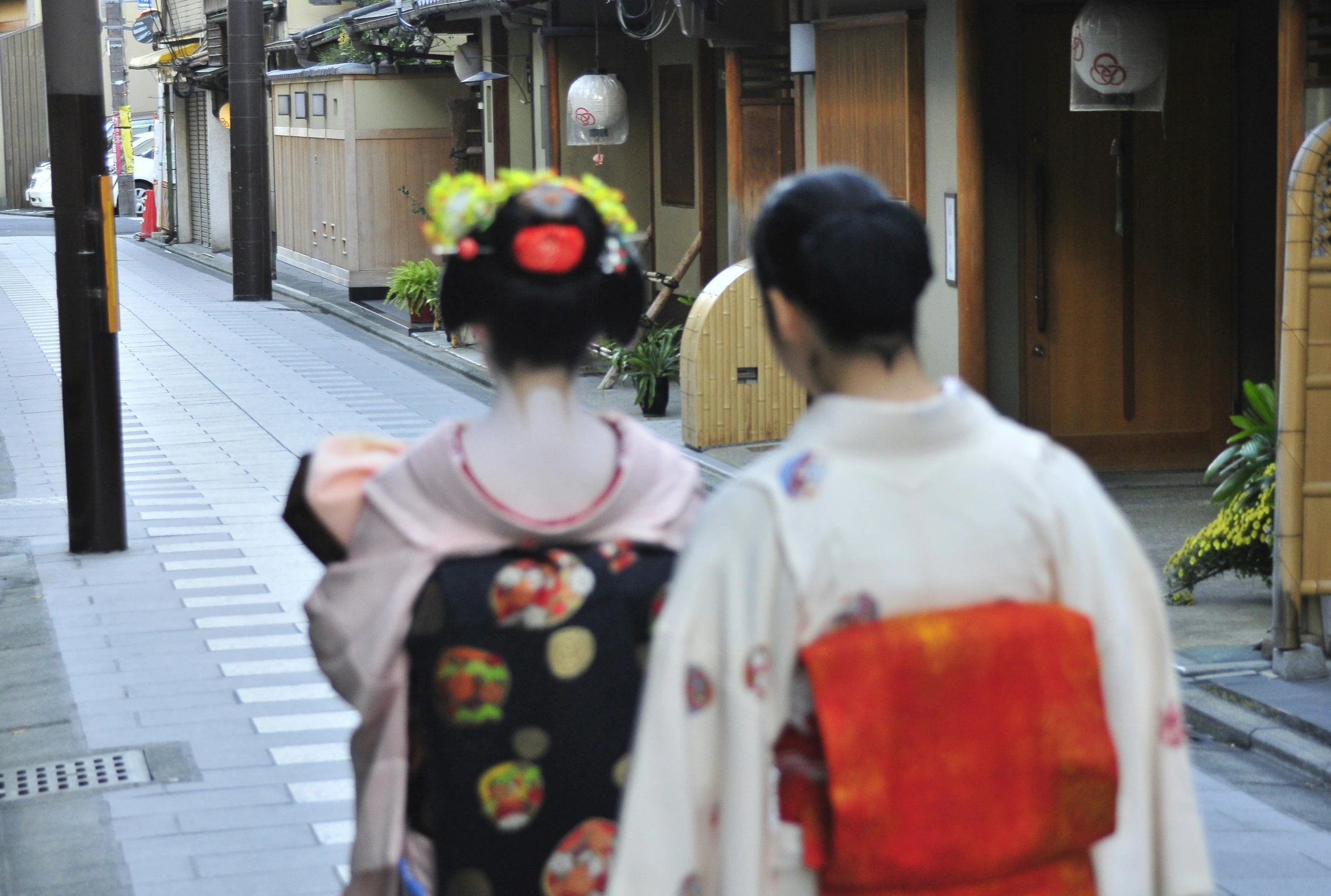 two geisha women wearing japanese outfits walk down a side street