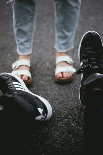 two people in sandals standing on asphalt and their feet are up