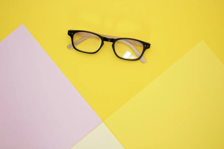 a pair of glasses with black frames sits on top of a yellow and pink wall