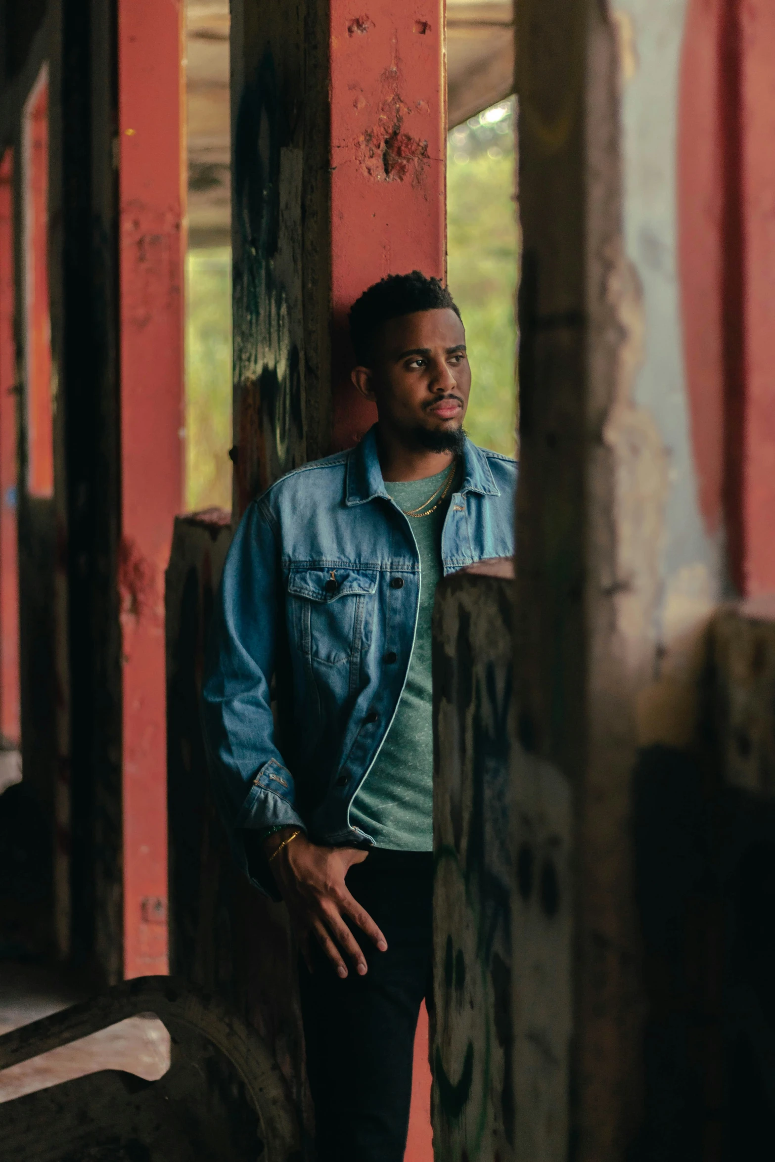 a man in a denim jacket leaning against a red wall