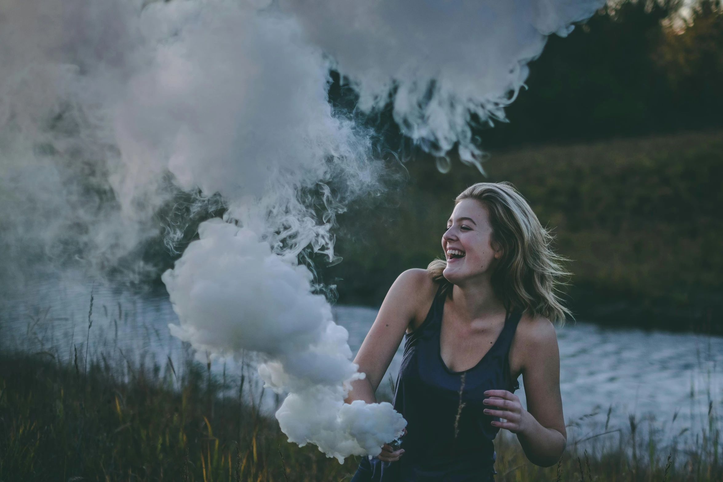 woman in black top laughing at a smoke machine near a river