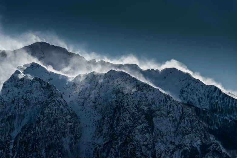 a mountain with snowy peaks under a cloudy sky