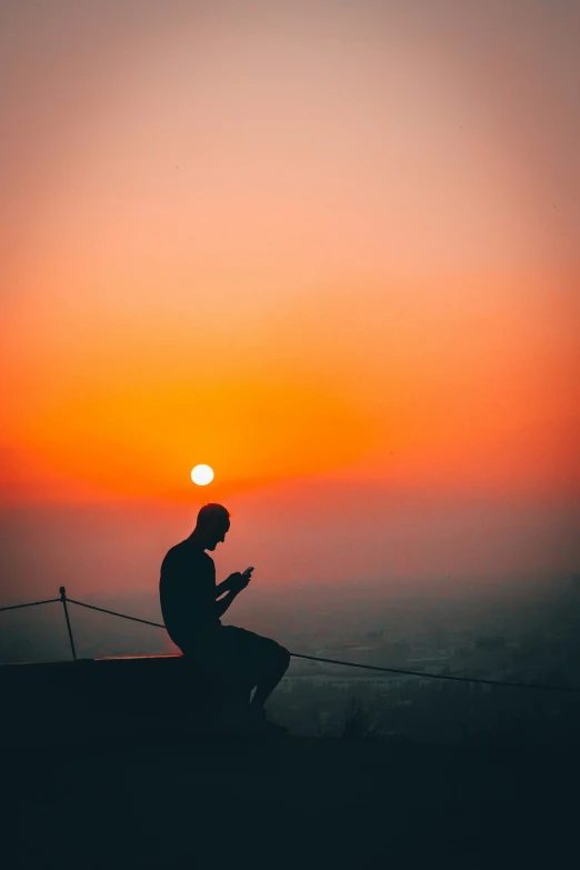 a person with his cellphone on a hill at sunset