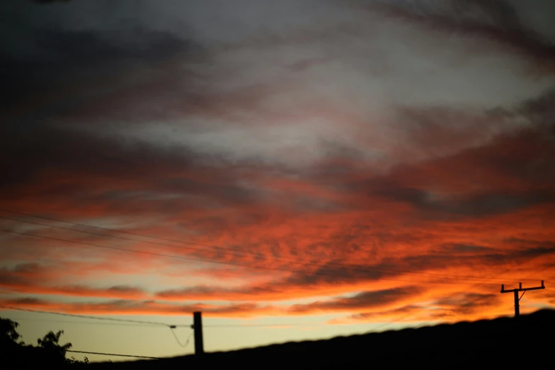 an orange and blue sunset with clouds and power lines