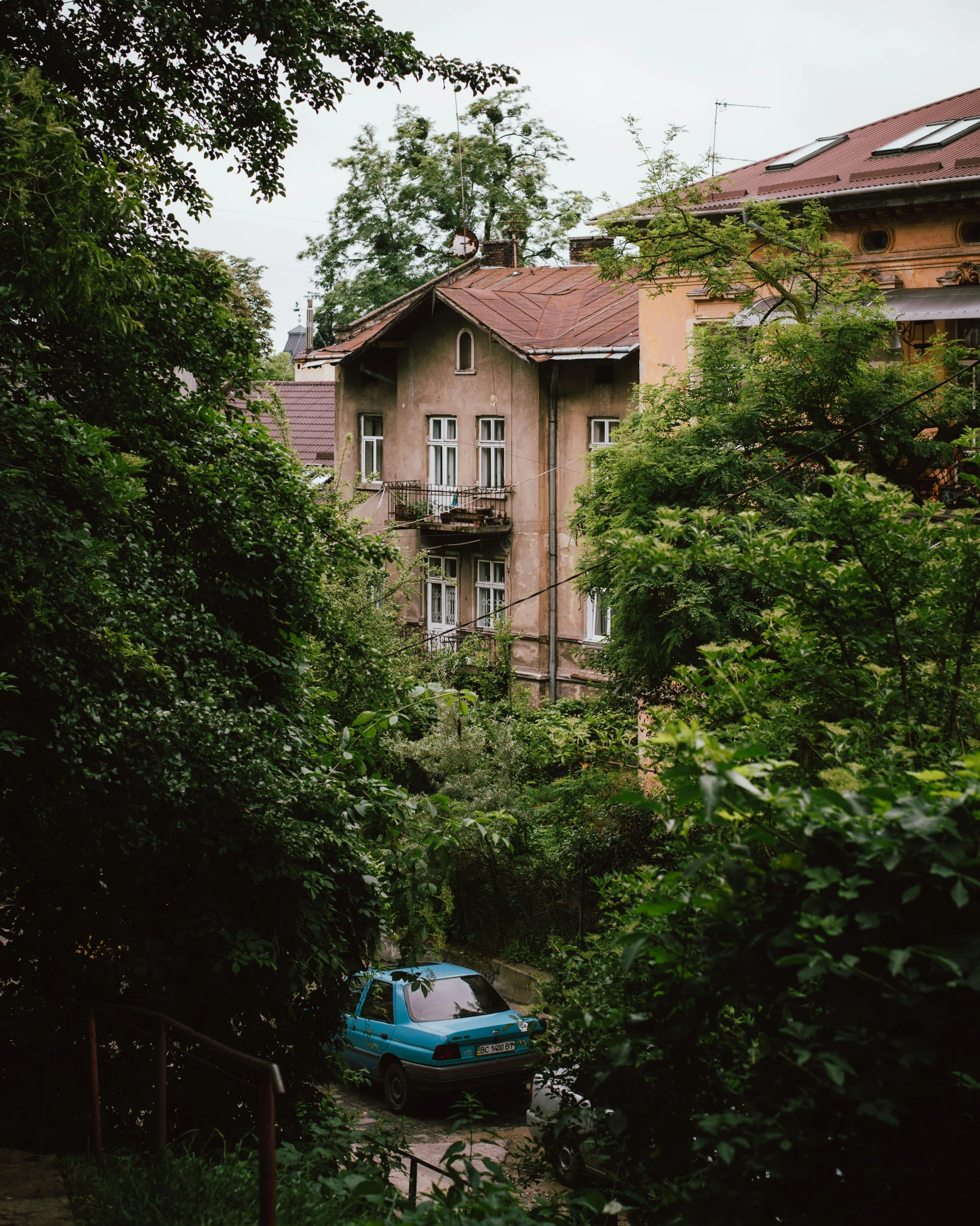 an old blue car is parked in front of a large house