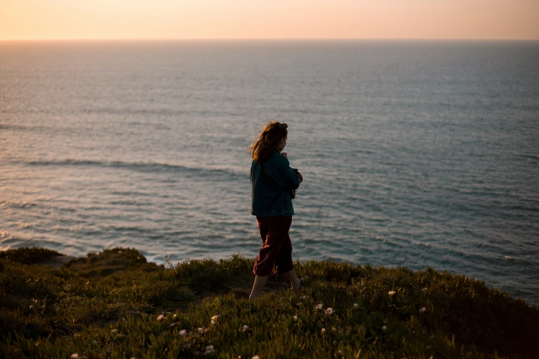 a woman is standing on the edge of a cliff overlooking water