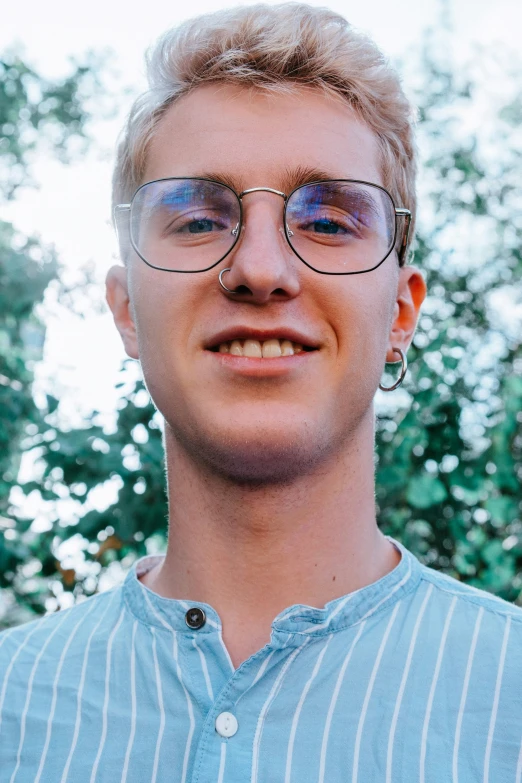 a young man in glasses with trees behind him