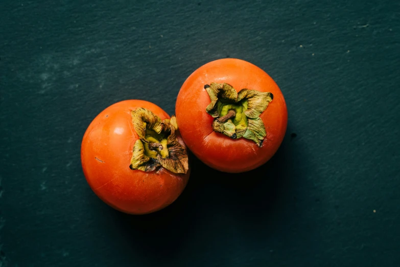 two ripe orange tomatoes are displayed on a table