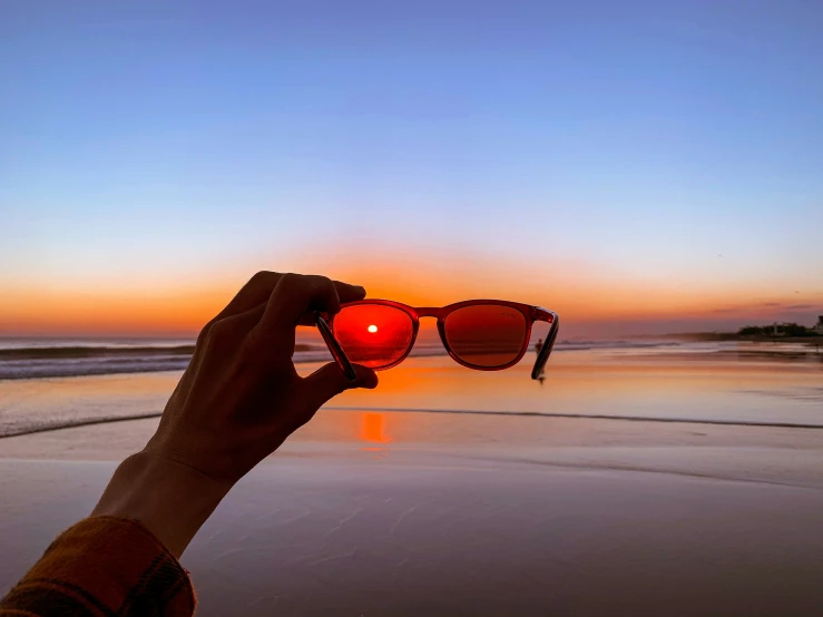a person holding their eye glasses while sun sets