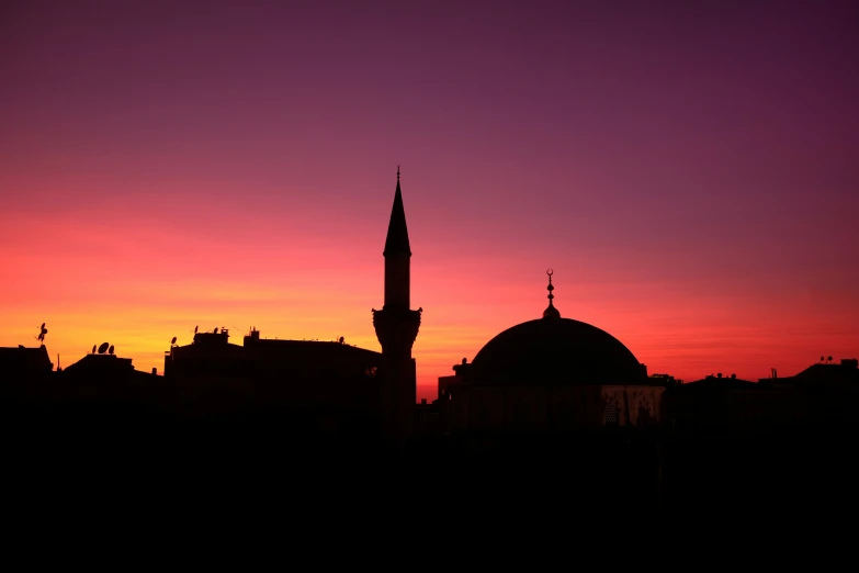 a silhouette of a building at sunset with pink and yellow clouds in the sky