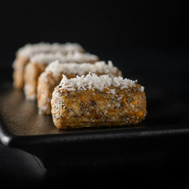 small pastries on a black plate, with white coconut