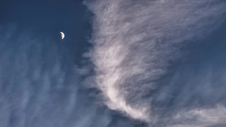 a white kite flies in a blue cloudy sky