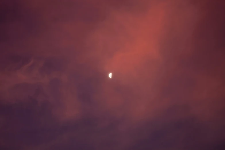 a po of the moon during the sunset with dark clouds in the background