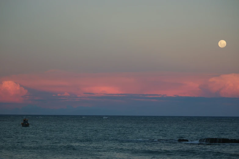 the moon is just beginning to shine at dusk over the ocean