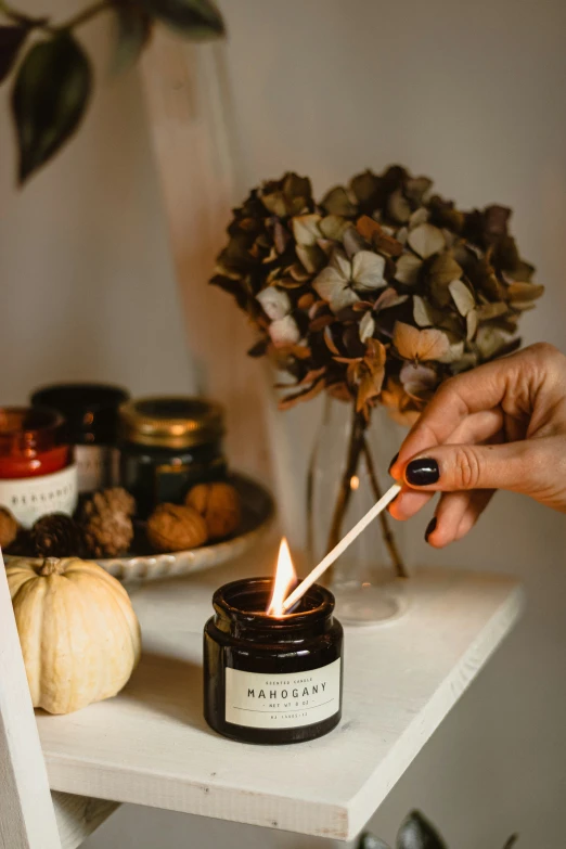 a person holding a burning candle next to a flower on a table