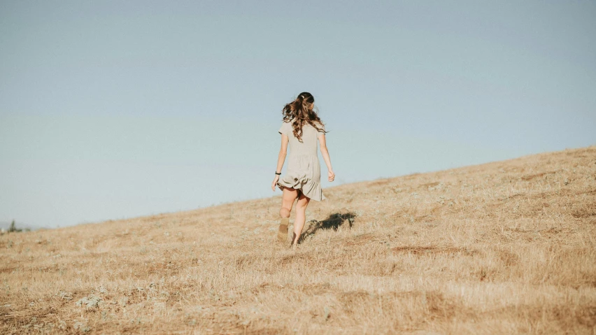 a woman walking across an empty hill with a suitcase in her hands