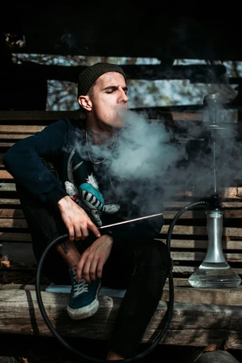 man sitting on wooden bench smoking an electronic cigarette